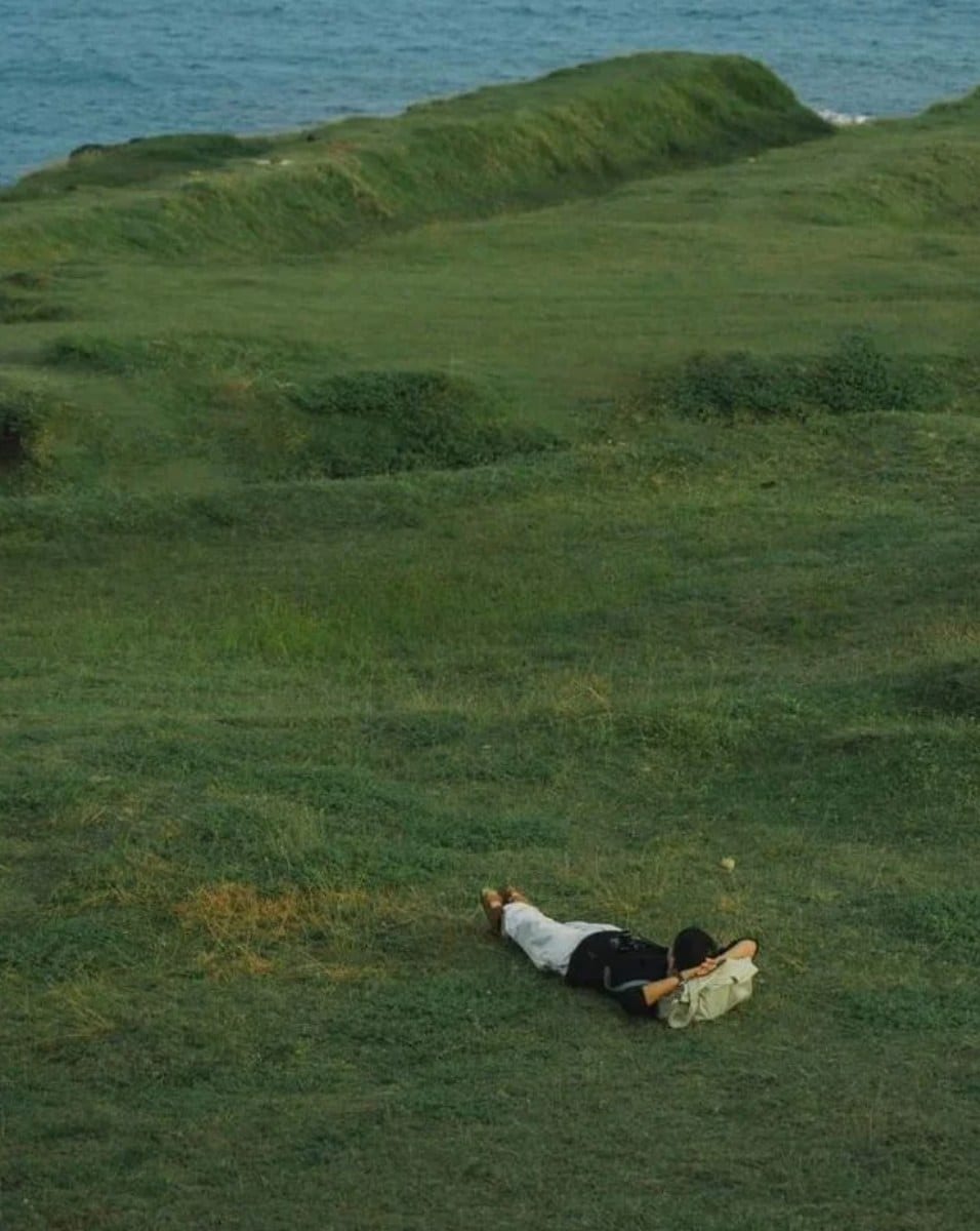 A person lying relaxed on a grassy field by the sea